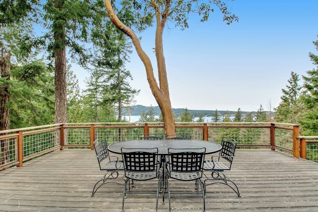 A wooden deck with a round table and four chairs, surrounded by a wooden railing, overlooking a natural landscape.