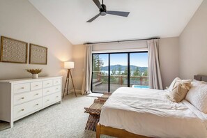 Ein Schlafzimmer mit Bett, Kommode, Deckenventilator, Fenster mit Vorhängen und Blick ins Freie.