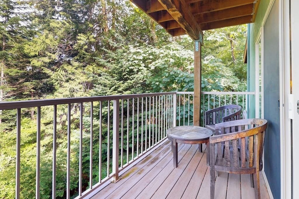 A wooden deck with a metal railing, two wooden chairs, and a view of a forested area.