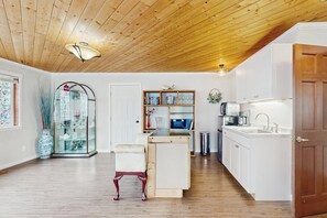 Ein geräumiger Raum mit Holzbalkendecke, einer Vitrine, einer weißen Bank und einer Küchenzeile mit weißen Schränken und einem Spülbecken.