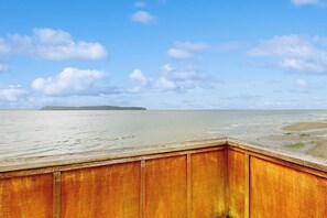 Eine Holzterrasse mit Blick auf einen Strand, bewölkter Himmel.