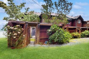 Ein zweistöckiges Holzhaus mit Veranda, Garage und einem kleinen Garten mit Blumen und Sträuchern.