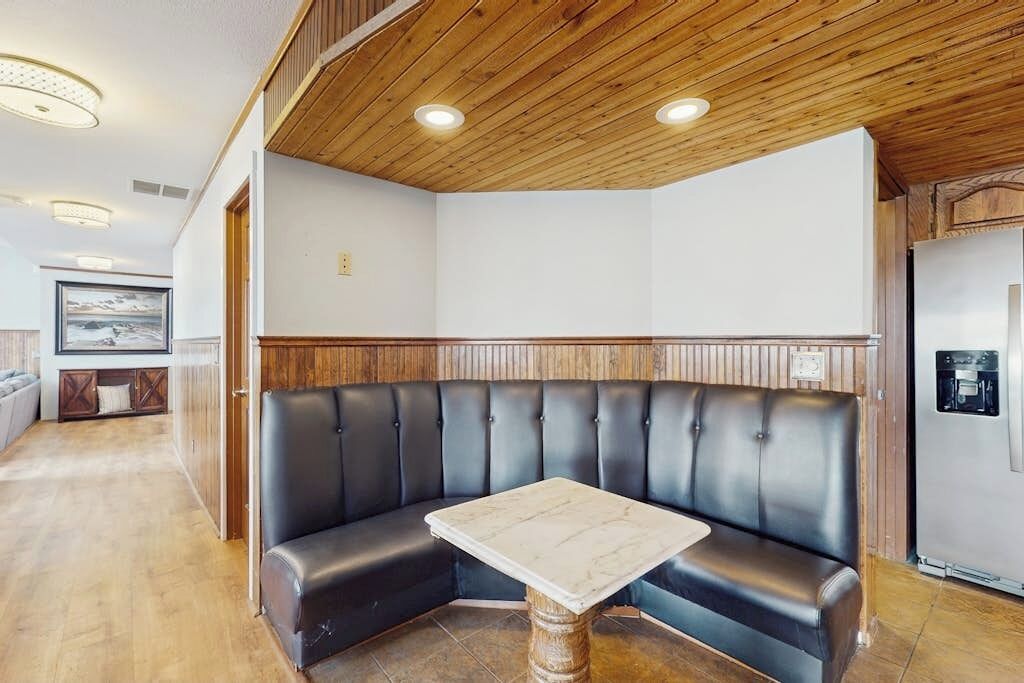 A corner seating area with a table, wooden ceiling, and a refrigerator.