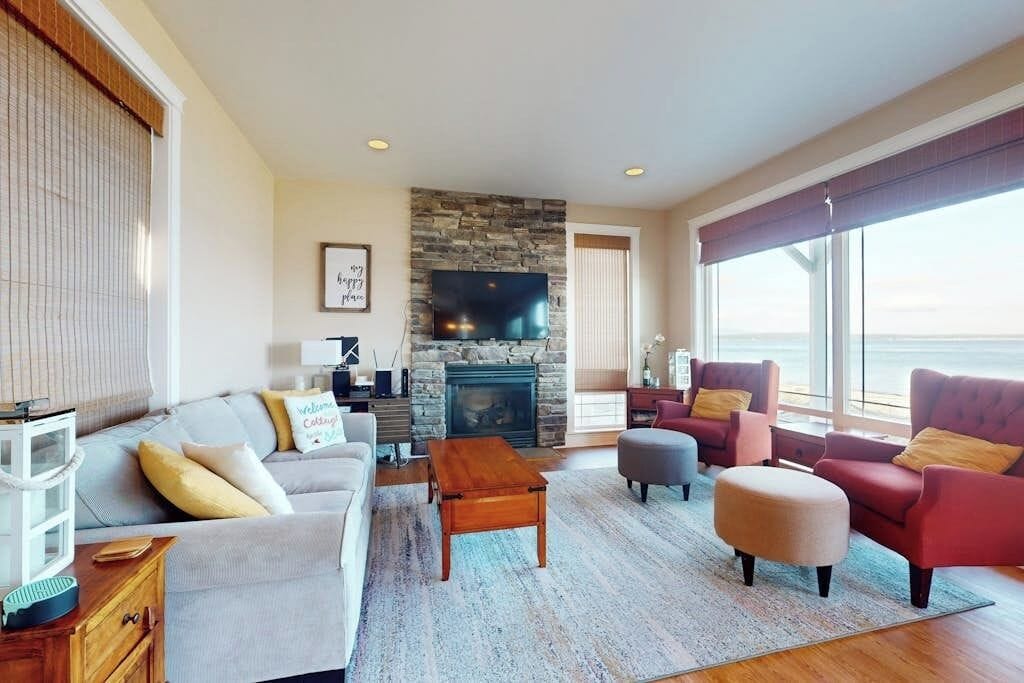 A living room with a stone fireplace, a television, and a large window overlooking the ocean.