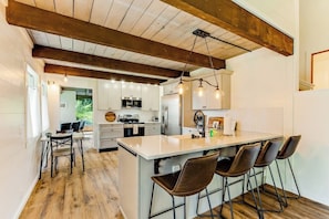 Una cocina moderna con armarios blancos, una isla central con taburetes de bar y vigas de madera a la vista en el techo.