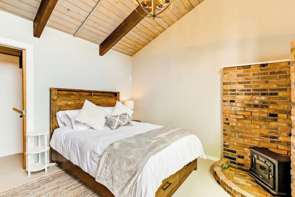 Un dormitorio con cama de madera, ropa de cama blanca, chimenea de ladrillo y una puerta blanca.