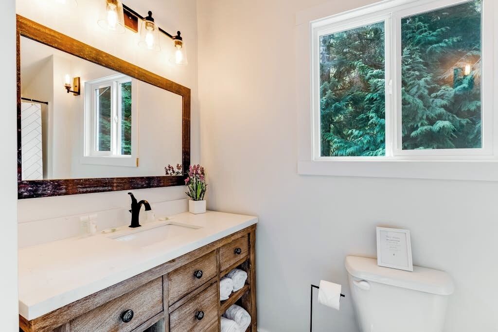 Un bagno con un lavandino bianco, un mobile vanità in legno e uno specchio grande.