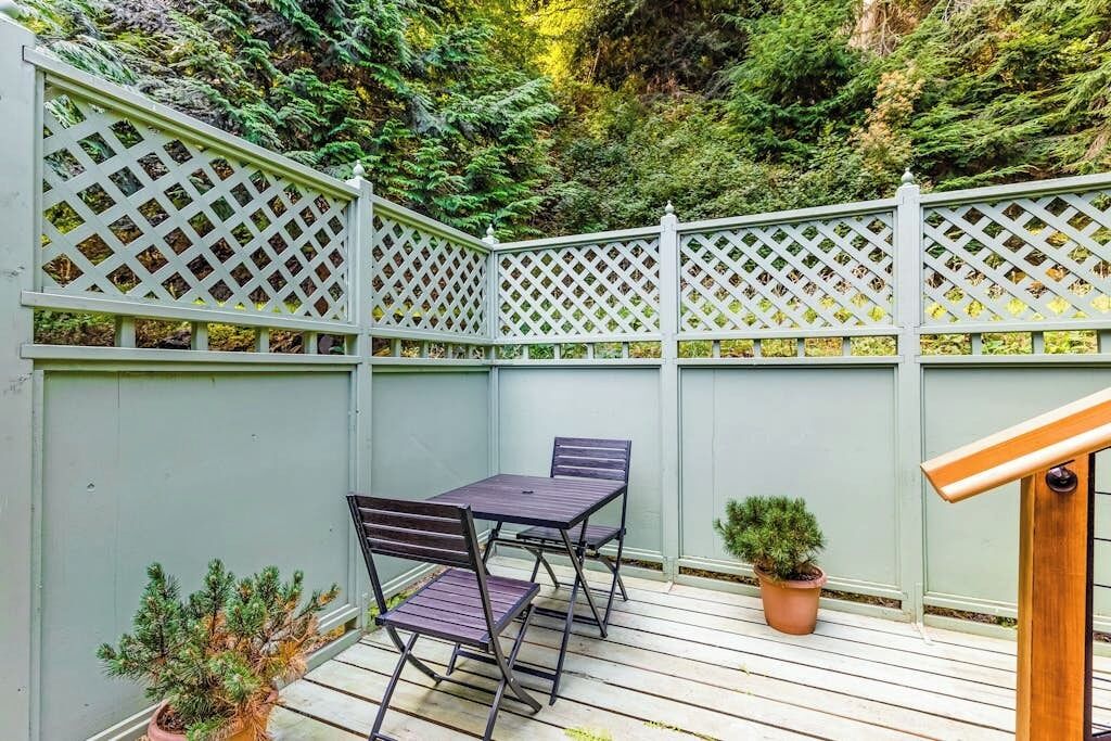 Eine Holzterrasse mit einem Gitterzaun, einem Tisch mit Stühlen und Blumentöpfen.