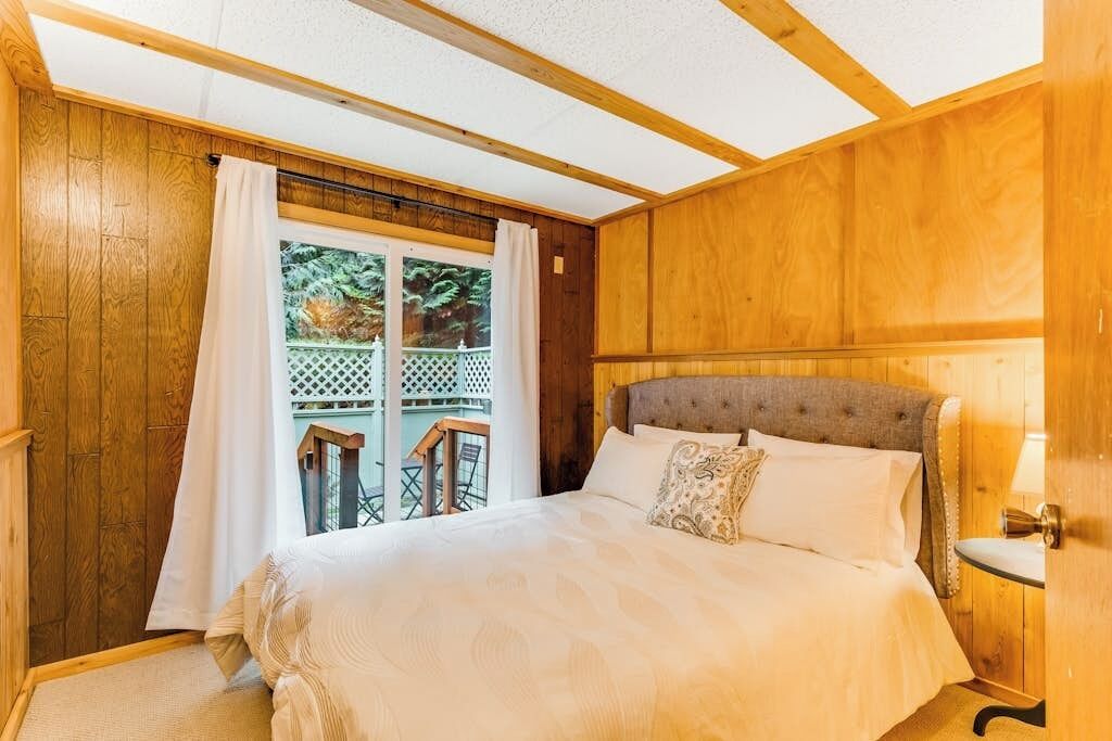 Un dormitorio con paneles de madera, una cama, una ventana con cortinas y vistas al exterior.