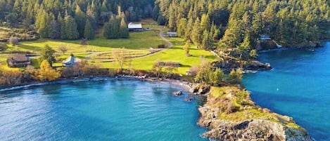 Rannalla sijaitseva kiinteistö, johon kuuluu suuri vesialue, metsäinen kukkula ja pieni rakennus.