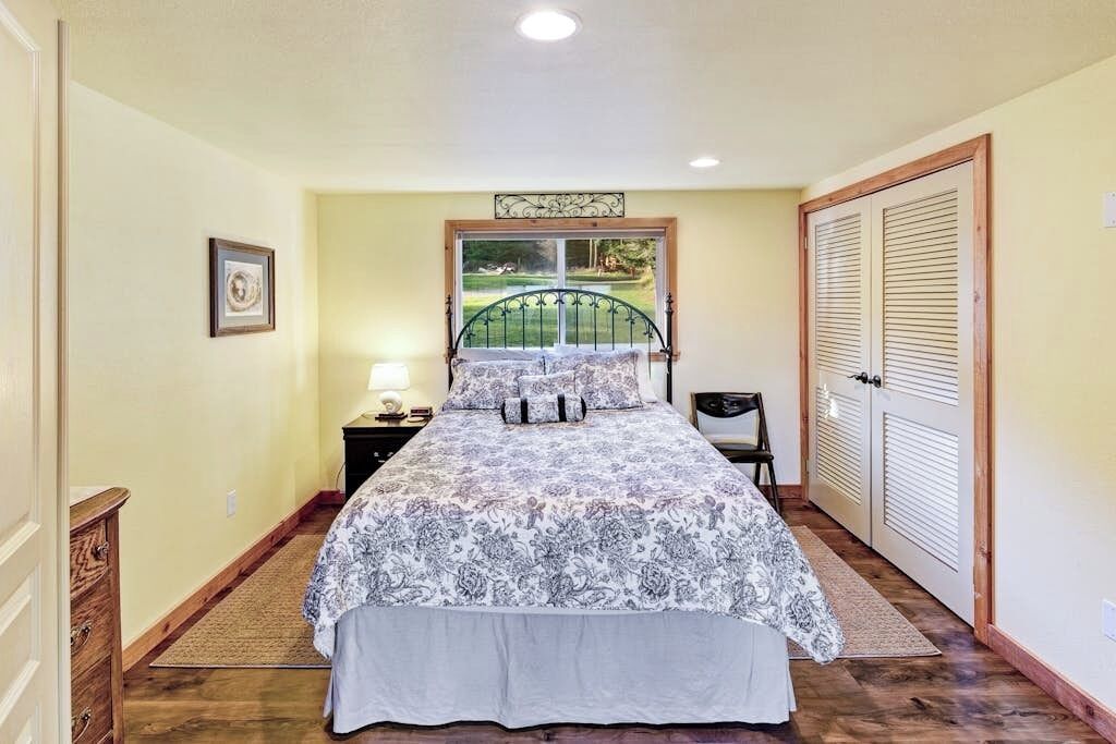 A bedroom with a bed, a nightstand, a dresser, a window with a view, and a door.