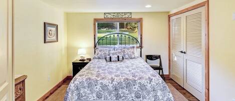 A bedroom with a bed, a nightstand, a dresser, a window with a view, and a door.