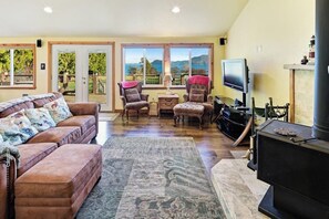 A living room with a sofa, armchairs, a television, a fireplace, and large windows with a view.