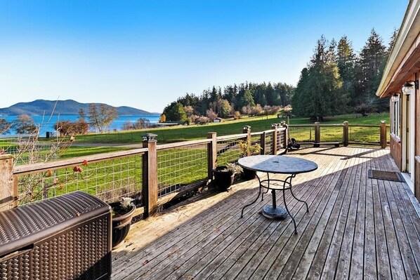 A wooden deck with a table and chairs, overlooking a lake and forested hills.