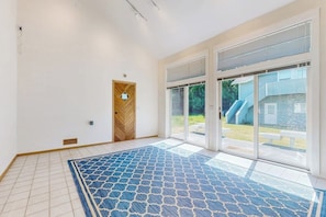 A spacious room with a patterned carpet, a wooden door, and large sliding glass doors leading to an outdoor area. - Charming Waterfront Home in Greenbank with Direct Beach Access and Stunning Ocean Views (Greenbank)