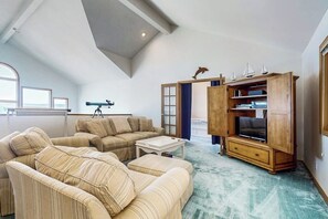 A high-ceilinged living room with a telescope, a large sofa set, and a wooden entertainment unit. - Charming Waterfront Home in Greenbank with Direct Beach Access and Stunning Ocean Views (Greenbank)