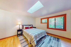A bedroom with a bed, a nightstand, a lamp, a skylight, and a window with a view of trees. - Peaceful 1BR Pet Friendly House Near Langley (Langley)