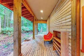 Eine Holzterrasse mit einem roten Stuhl und Regalen, umgeben von einem Wald.