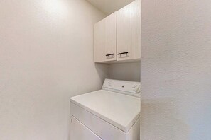 A compact laundry room with a front-loading washer and dryer, wooden cabinets above, and a plain wall. - Peaceful 1BR Pet Friendly House Near Langley (Langley)