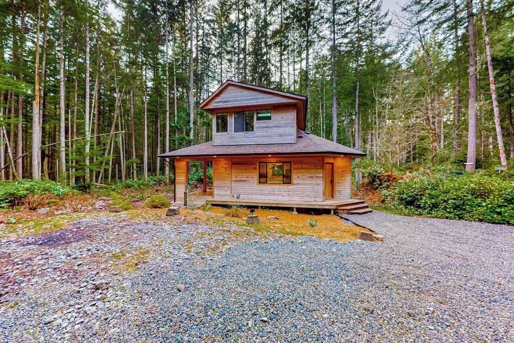 A two-story cabin with a sloped roof, surrounded by a forest.