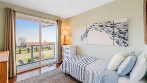 Un dormitorio con cama, una mesita de noche, una lámpara y vistas a través de un ventanal corredero.