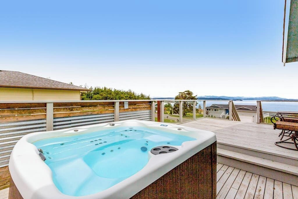 A hot tub on a wooden deck with a view of a body of water and distant mountains.