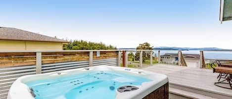 A hot tub on a wooden deck with a view of a body of water and distant mountains.