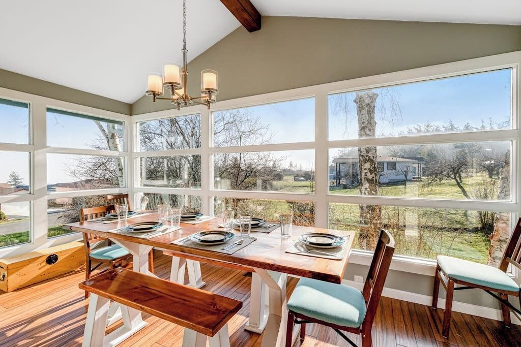 A dining area with a wooden table set for four, large windows, and a view of the outdoors.