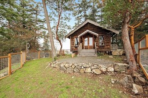 Una cabaña rústica con base de piedra, terraza de madera y zona vallada.