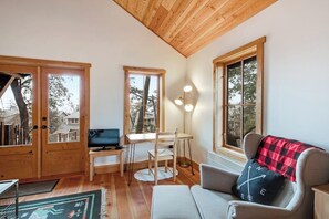 A cozy room with a wooden ceiling, a desk with a computer, a chair, a sofa, and a large window. - Secluded and Stylish Cabin in Eastsound Near Beach and Town (Eastsound)