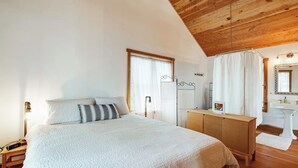 Ein Schlafzimmer mit einem Bett, einem Nachttisch, einer Lampe und einer Holzbalkendecke.
