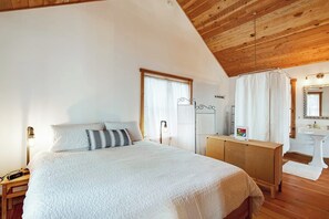 A bedroom with a bed, bedside table, lamp, and a wooden ceiling. - Secluded and Stylish Cabin in Eastsound Near Beach and Town (Eastsound)