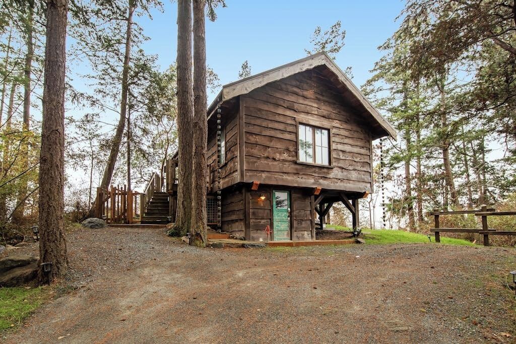 A rustic cabin with a wooden exterior, a front porch, and a staircase leading to a deck.