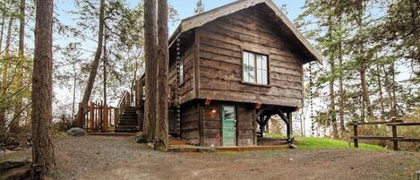 A rustic cabin with a wooden exterior, a front porch, and a staircase leading to a deck.