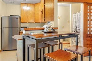A kitchen with wooden cabinets, a stainless steel refrigerator, a wooden table with chairs, and a small island with a sink.