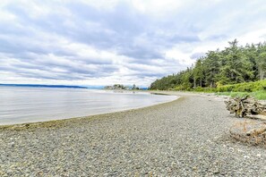 Une plage de galets bordée d’une zone boisée et donnant sur une étendue d’eau.