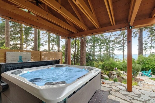 A hot tub under a wooden pergola with a view of trees and a body of water.