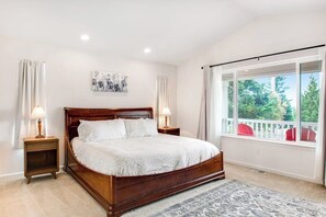 Une chambre avec un grand lit, deux tables de chevet avec des lampes, une fenêtre donnant sur des arbres et un tableau au mur.