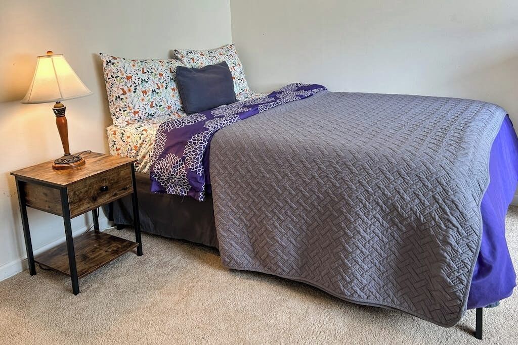 A bedroom with a bed, a nightstand, a lamp, and a patterned pillow.