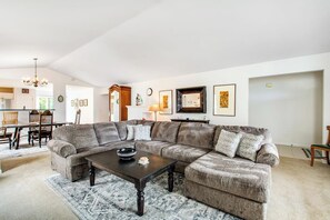 Un salon spacieux comprenant un canapé d’angle, une table basse et un coin repas avec des chaises et une table.