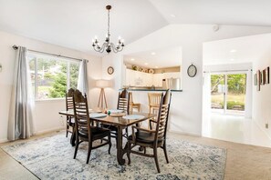 Ein Essbereich mit einer Chandelier, einem Tisch für vier Personen und Blick auf die Küche und den Garten durch das Fenster.