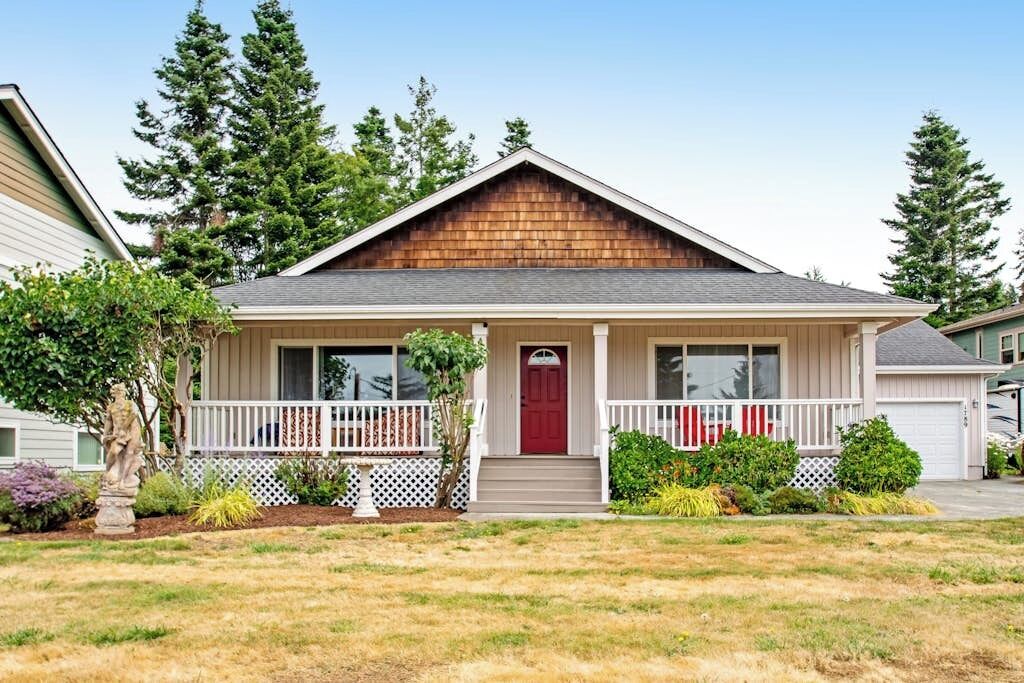 A single-story house with a front porch, a red door, and a small front yard with landscaping.