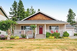 Ein eingeschossiges Haus mit Veranda, einer roten Tür und einem kleinen Vorgarten mit Bepflanzung.