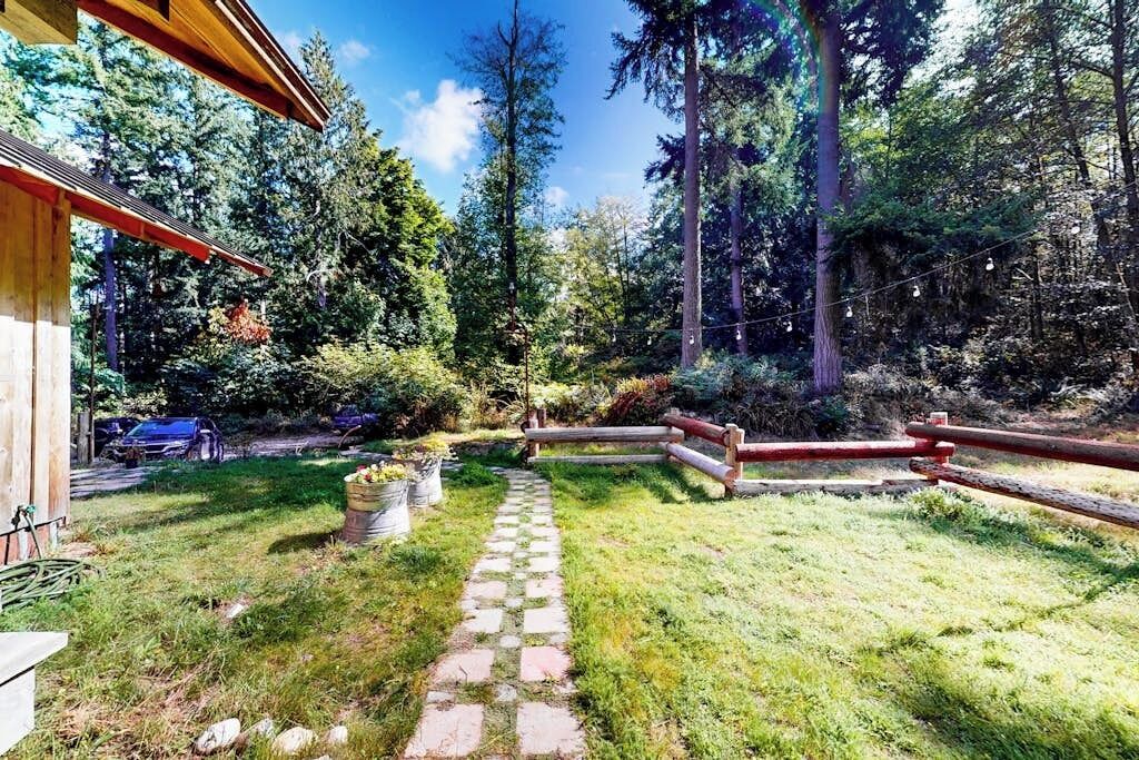 A wooden cabin with a stone pathway leading to a wooden deck, surrounded by a forested area.