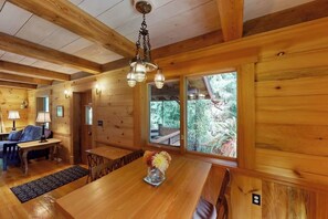 Interno di una baita in legno con un tavolo da pranzo, sedie, un divano e un lampadario.