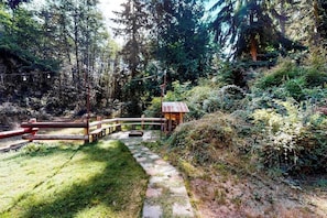 Una zona boschiva con un ponte di legno, un piccolo riparo e un sentiero in pietra.