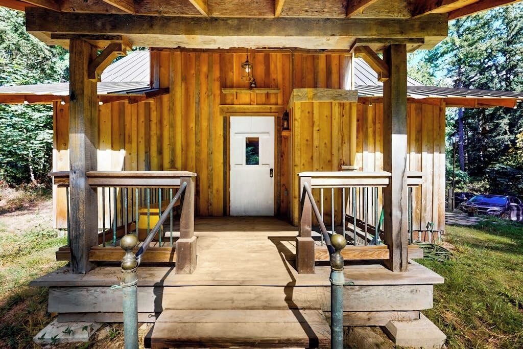 A wooden cabin with a porch, a door, and a staircase leading to a platform.