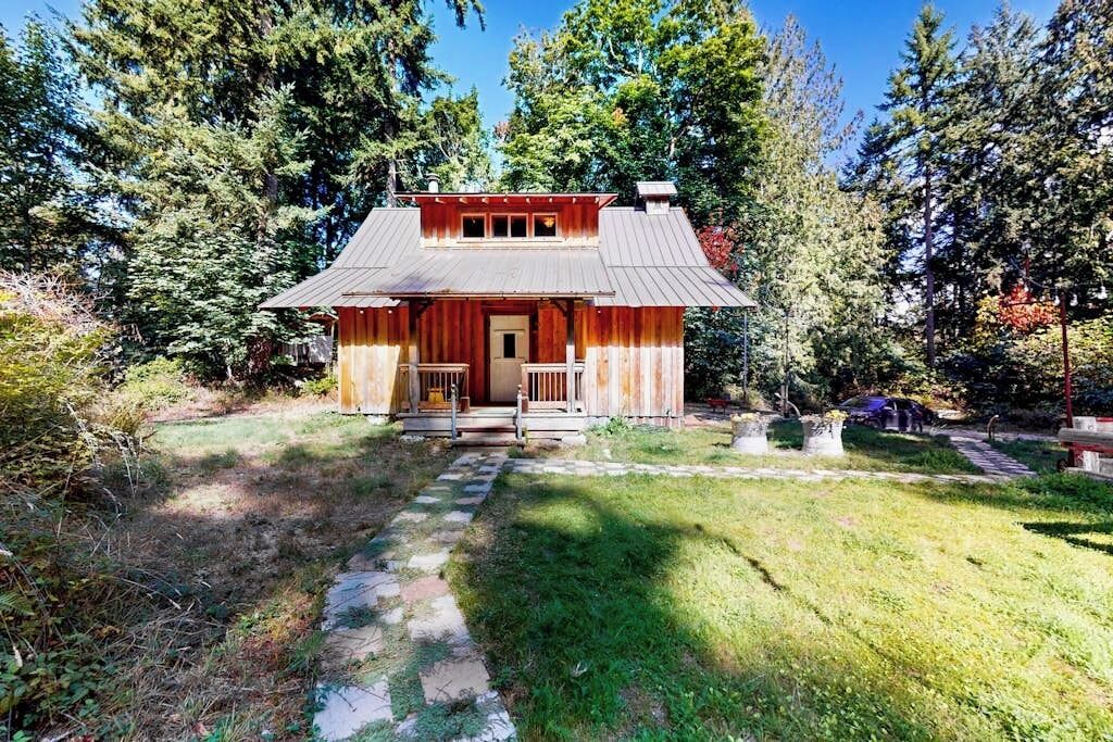 Un chalet rustique doté d’un porche, entouré d’arbres et accessible par un sentier de pierres menant à l’entrée.