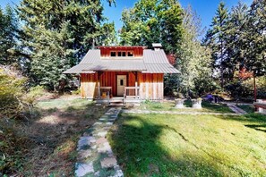 A rustic cabin with a porch, surrounded by trees and a stone pathway leading to the entrance.