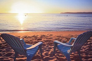 Zwei Strandstühle mit Blick auf den Ozean, im Hintergrund ein Sonnenuntergang.